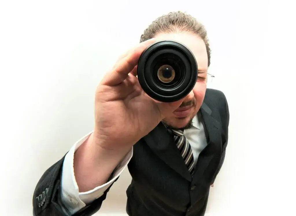 Man in a suit looking through a camera lens, his eye magnified by the glass