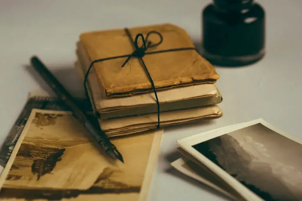 Old photographs, notebooks tied with string, a fountain pen and an ink bottle on a light table