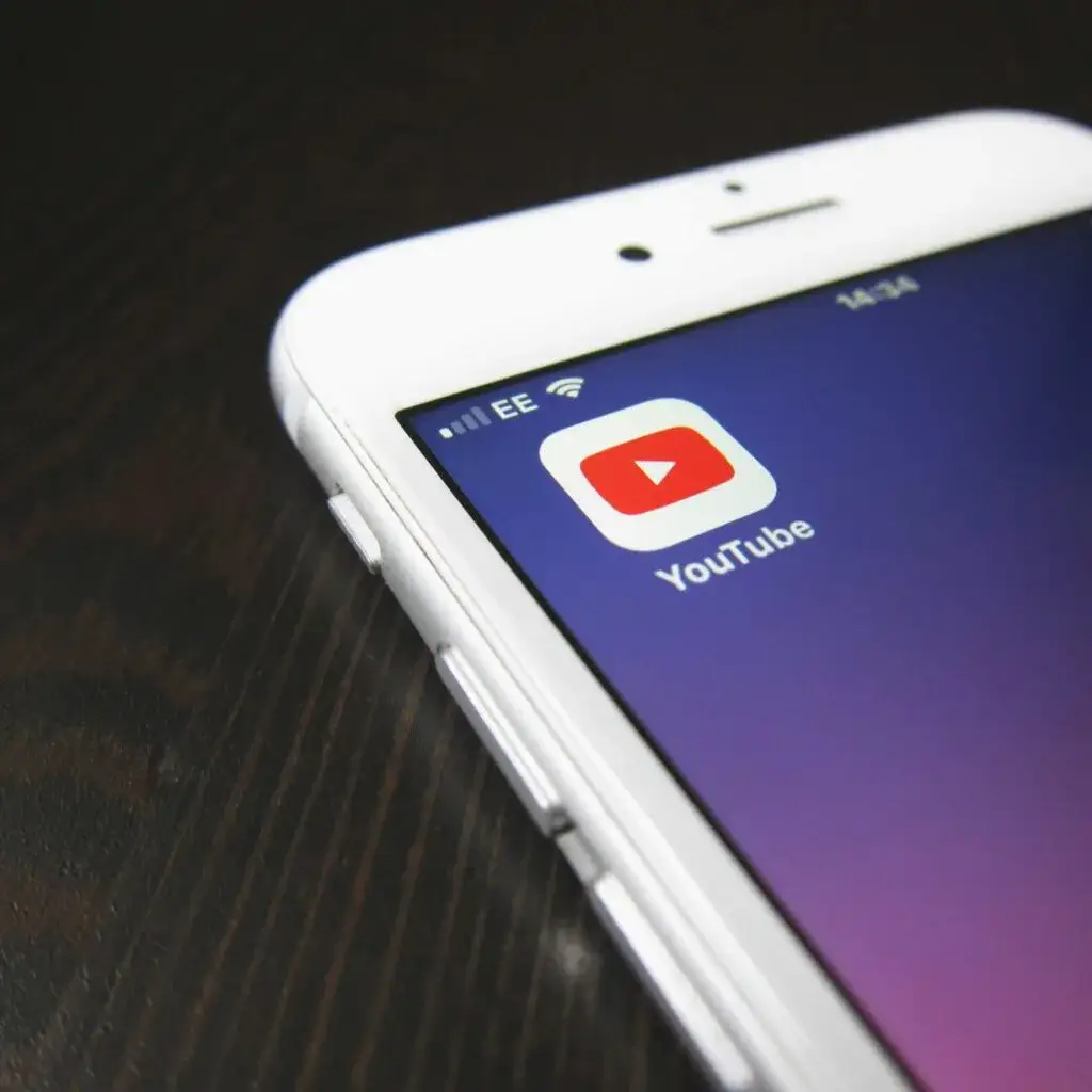 Corner of a white phone on a dark wooden table, with the YouTube app icon on screen